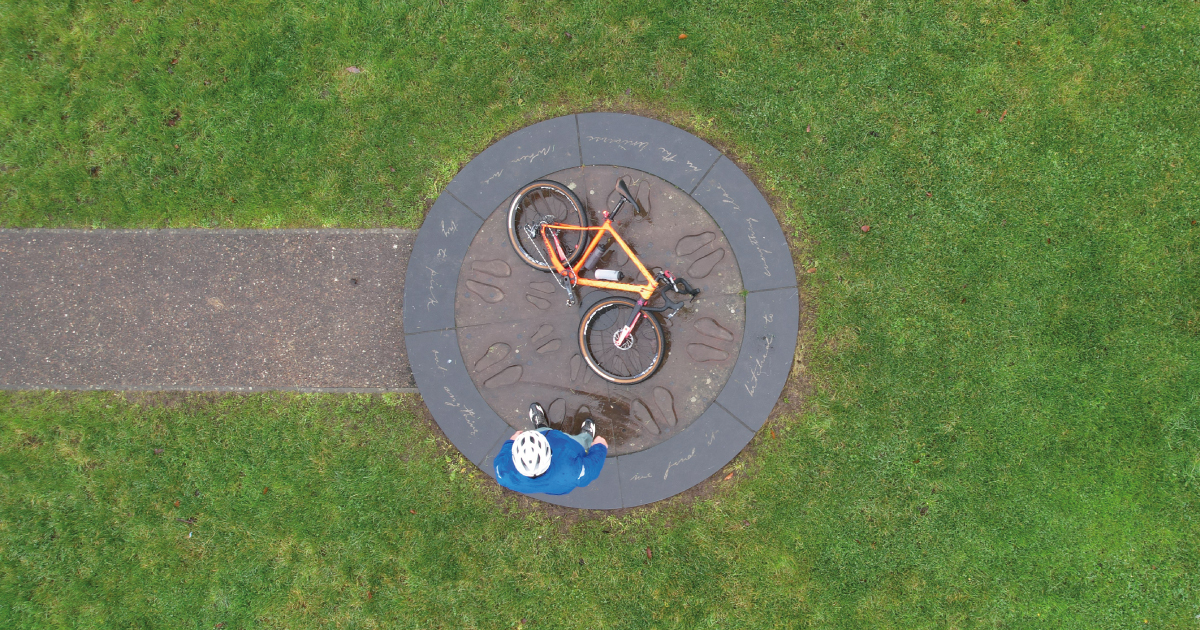 Aerial view of John Muir Way Marker with a cyclist standing in front of their bike lying on the stone paved circle
